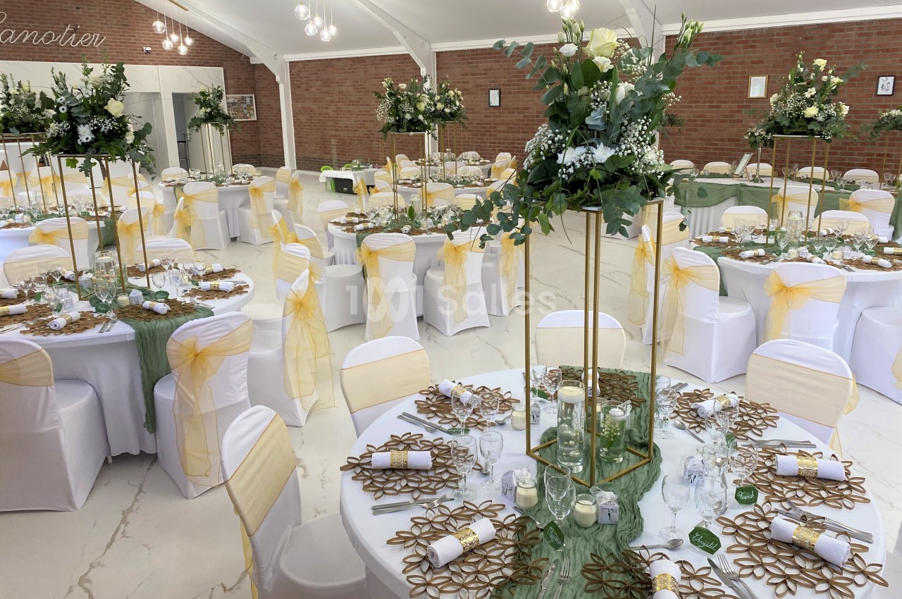 Salle de réception décorée avec des tables rondes, nappes blanches, chemins de table verts et centres de table fleuris.