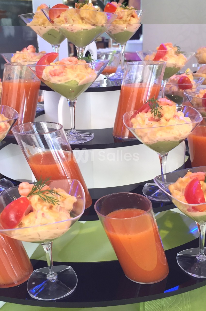 Présentoir avec verrines de soupe rouge, crevettes, avocat et tomates cerises, disposées sur plusieurs niveaux.