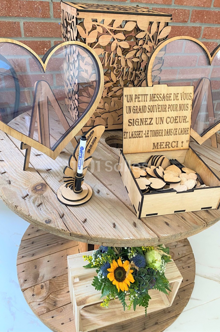 Boîte en bois pour messages de mariage, avec cœurs à signer, posée sur une table ronde en bois, décorée de fleurs.