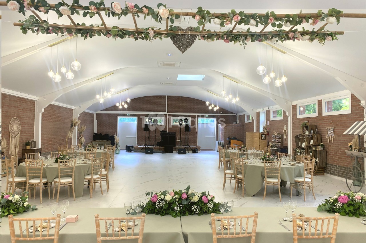 Salle de réception décorée avec des tables dressées, des chaises en bois clair et des guirlandes florales suspendues.