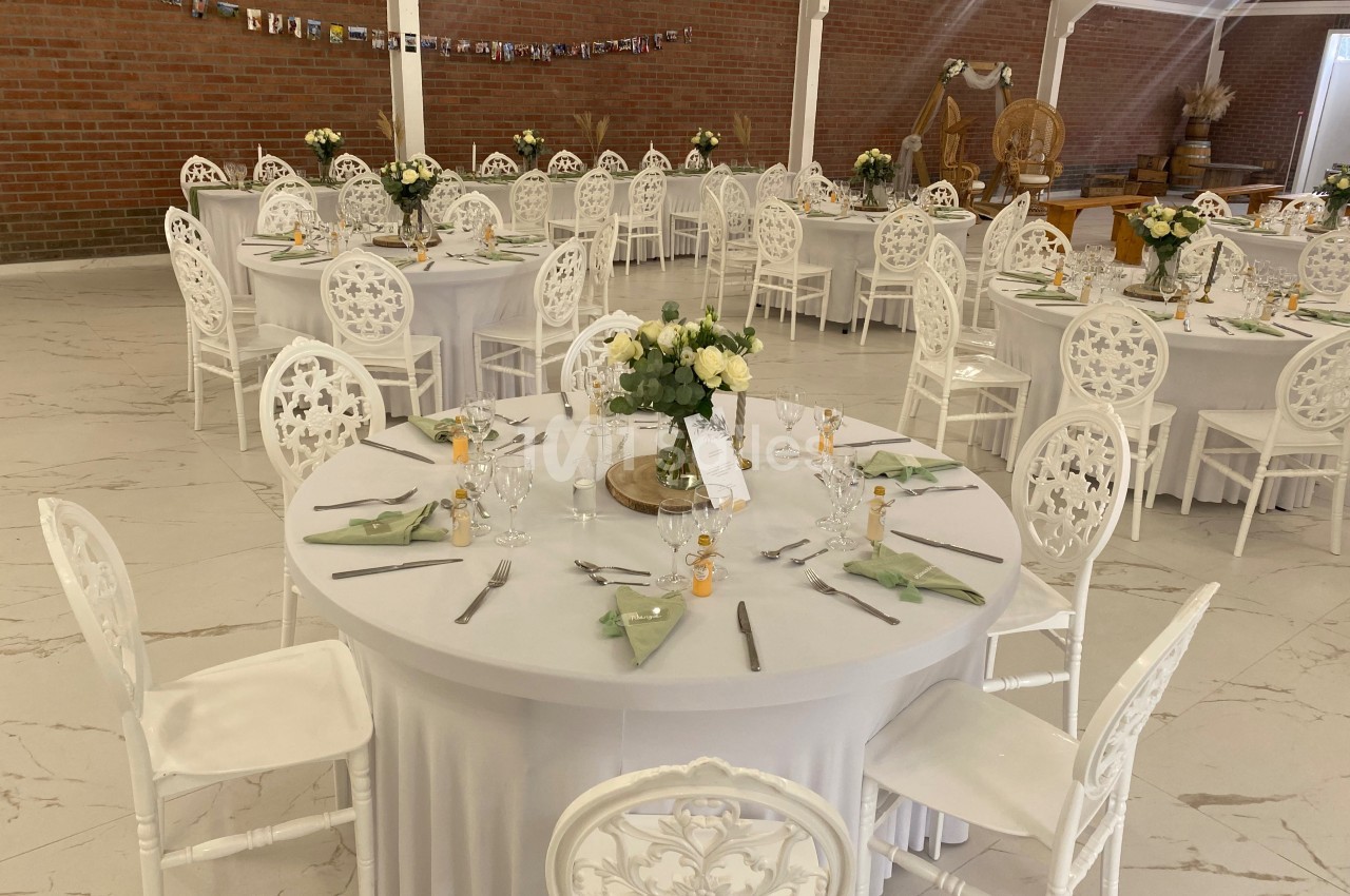 Salle de réception décorée avec des tables rondes dressées, nappes blanches, chaises assorties et centres de table fleuris.