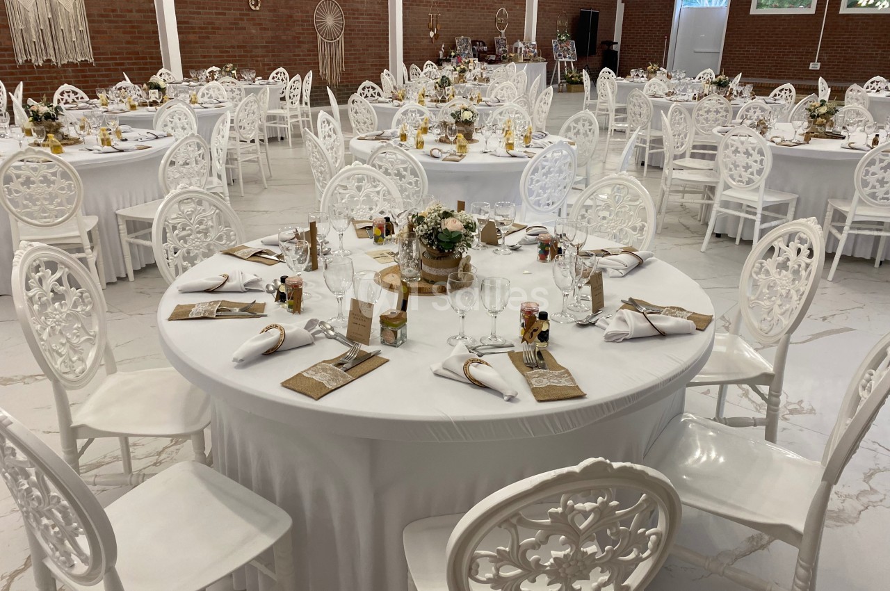 Salle de réception décorée avec des tables rondes blanches, nappes élégantes et chaises assorties, prête pour un événement.