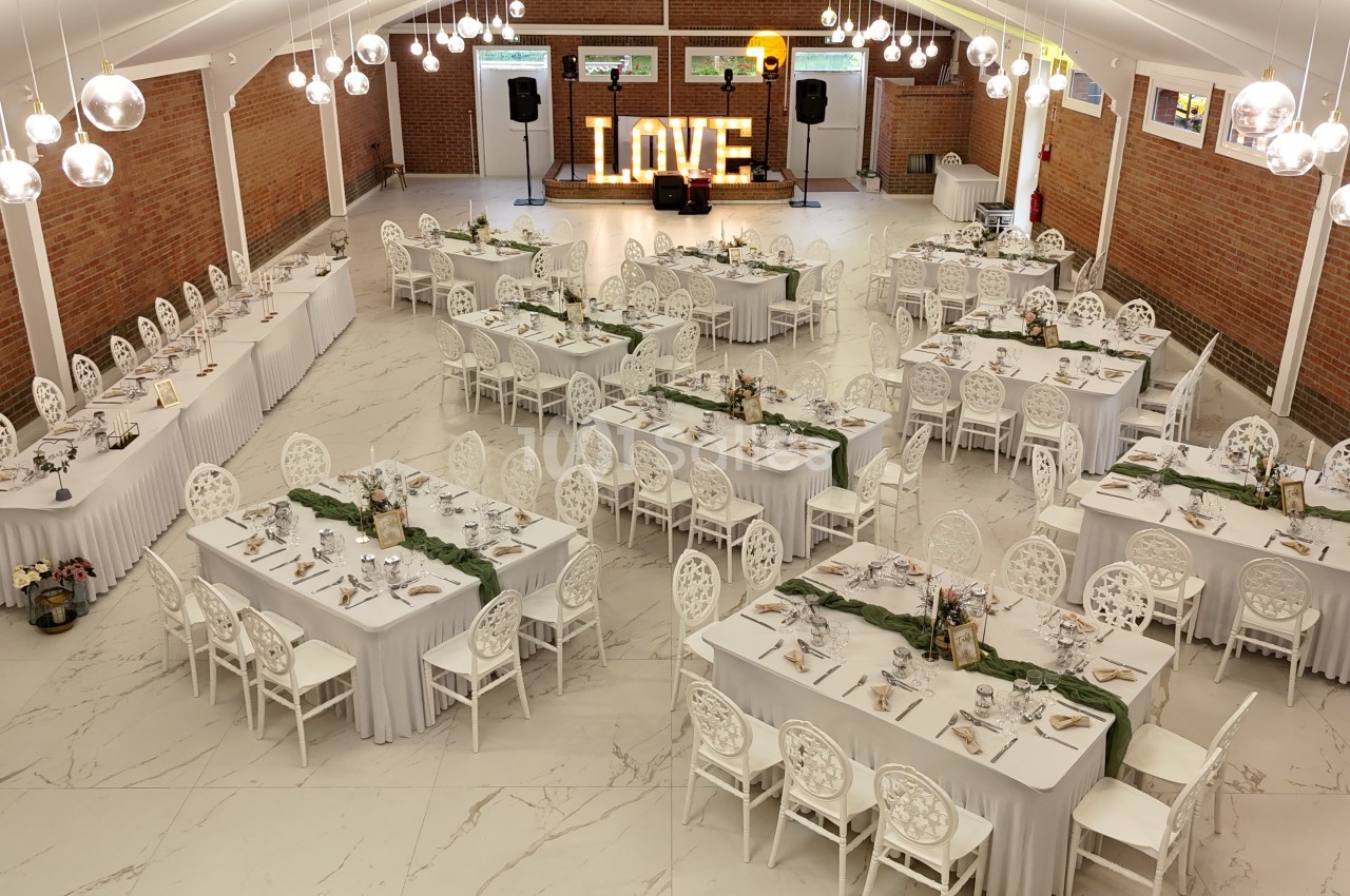 Salle de réception décorée pour un événement, avec des tables alignées, nappes blanches et une enseigne lumineuse ’LOVE’.