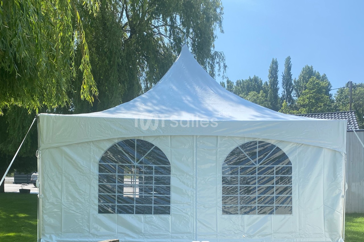 Tente blanche avec fenêtres en arc installée dans un jardin, entourée d'arbres et de pelouses sous un ciel dégagé.