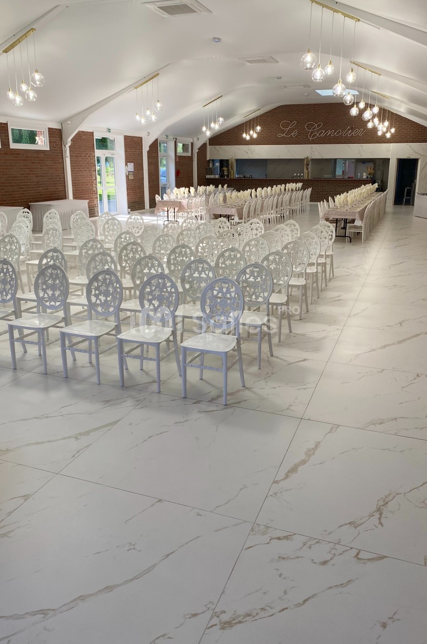 Salle de réception lumineuse avec des rangées de chaises blanches décoratives et un sol en carrelage effet marbre.