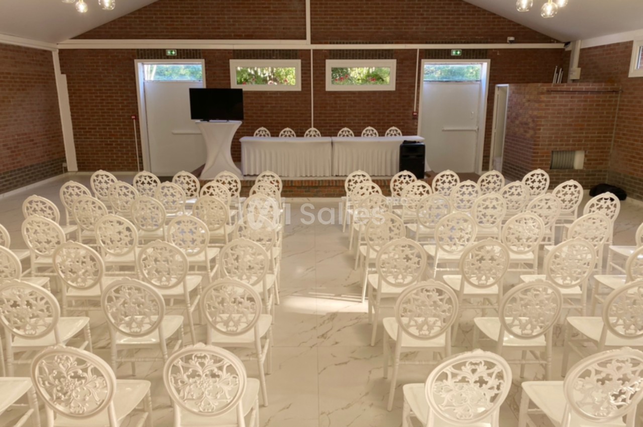 Salle de conférence lumineuse avec des rangées de chaises blanches devant une table et un écran.