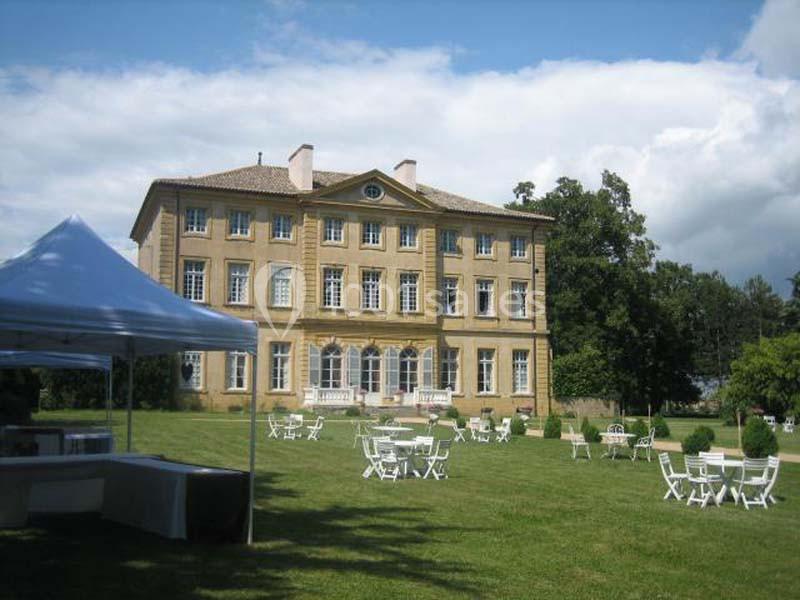 Façade d'un grand bâtiment ancien entouré d'un jardin avec des tables et chaises blanches disposées sur la pelouse.
