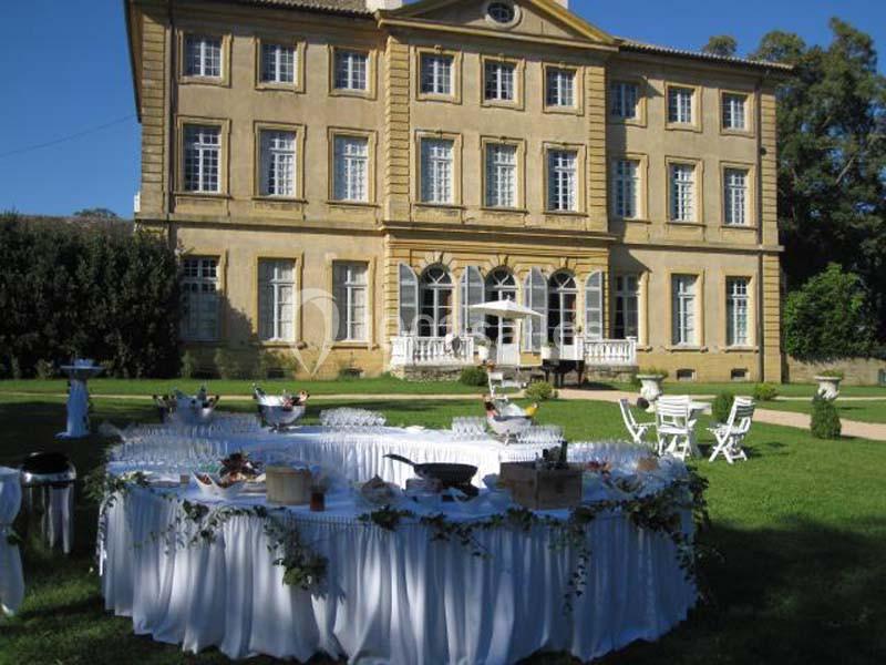Table ronde décorée pour un événement en plein air devant un grand bâtiment historique avec jardin.