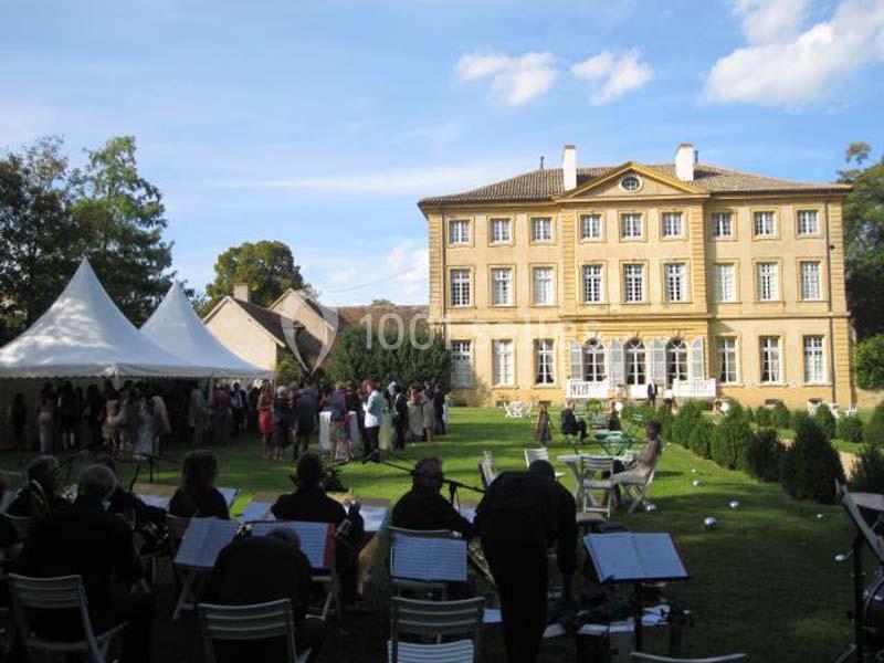 Un manoir en pierre avec un jardin, des tentes blanches et des personnes rassemblées lors d'un événement en plein air.