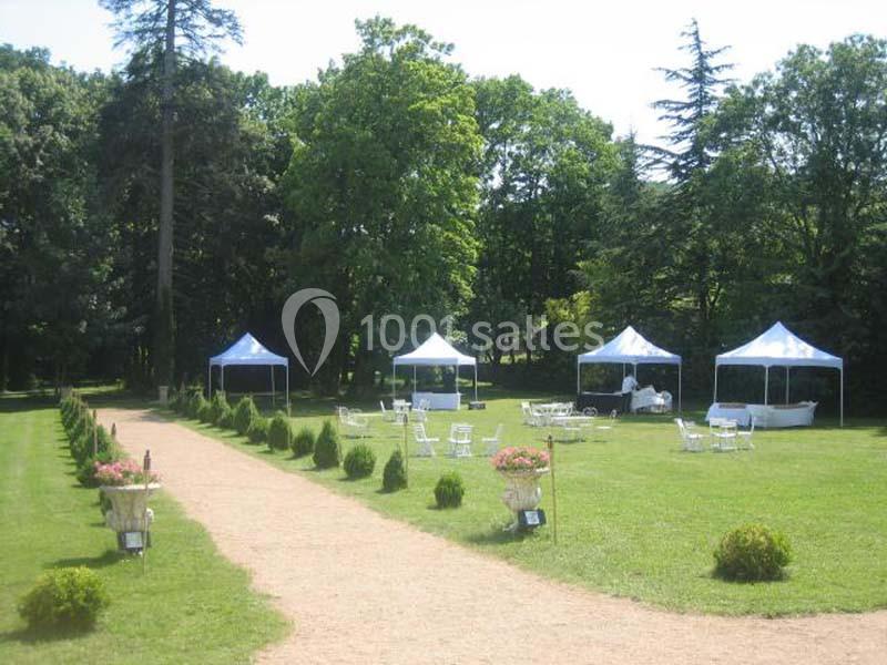 Allée centrale bordée de pelouse et buissons, menant à des tentes blanches installées dans un parc arboré.