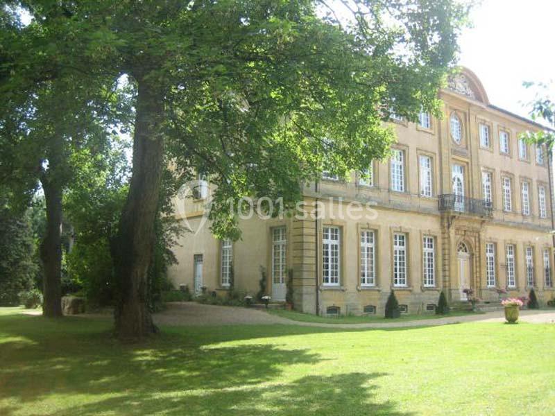 Façade d'un bâtiment ancien entouré d'arbres et donnant sur une pelouse verdoyante.