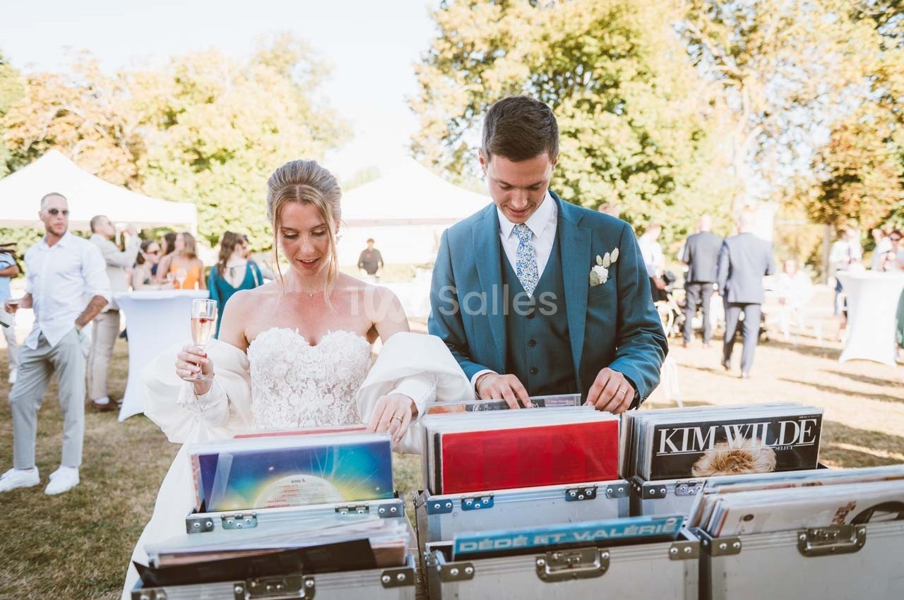 Un couple en tenue de mariage feuillette des vinyles lors d'une réception en plein air par une journée ensoleillée.
