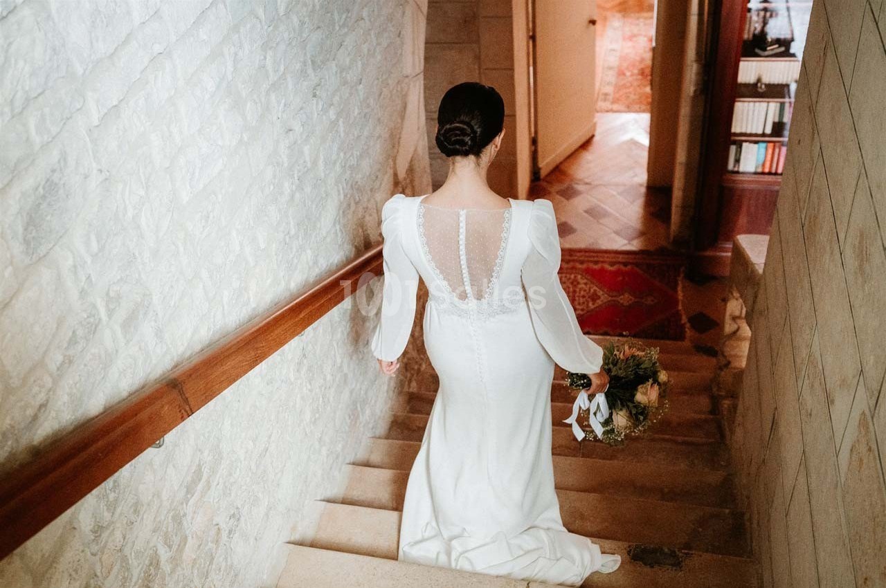Une femme en robe de mariée blanche descend un escalier en pierre, tenant un bouquet de fleurs.