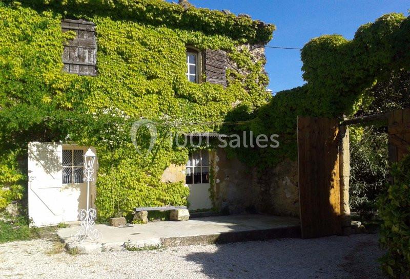 Façade d'une maison en pierre recouverte de vigne vierge, avec une cour en gravier et un portail en bois.