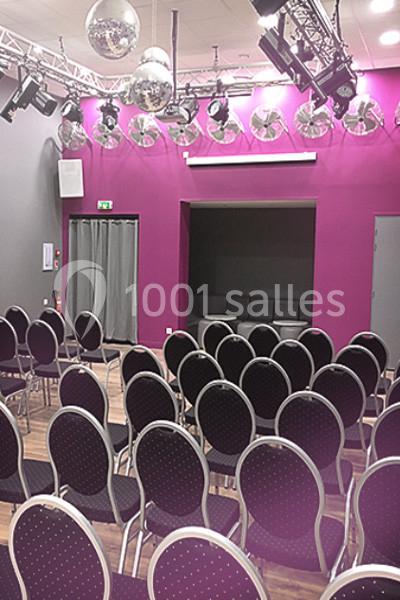 Salle de conférence avec rangées de chaises noires, murs violets et éclairage suspendu avec boules à facettes.