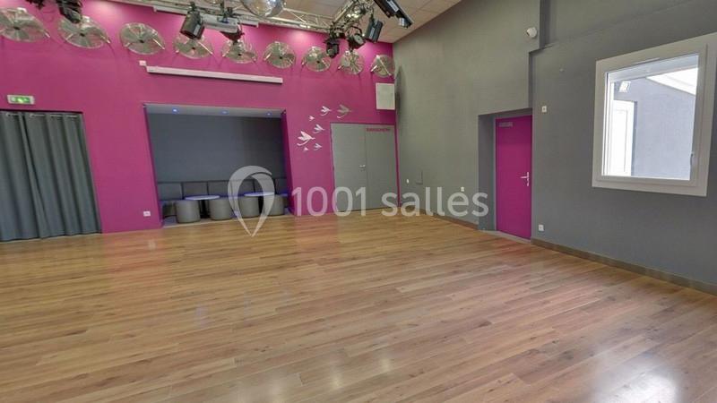 Salle avec parquet, murs roses et gris, sièges dans un coin, éclairage au plafond et décorations murales d'oiseaux.