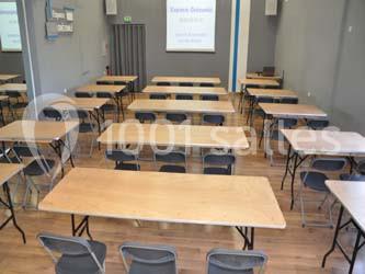 Salle de réunion avec des tables en bois clair et des chaises pliantes, prête pour une présentation ou une formation.