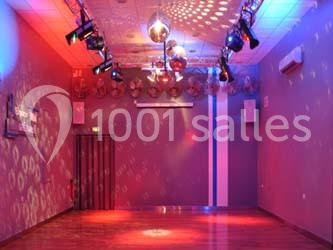 Salle de danse vide avec éclairage coloré, boules à facettes suspendues et parquet au sol.