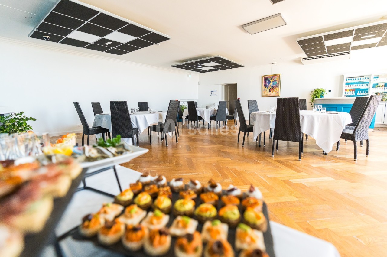 Salle de restaurant lumineuse avec tables dressées et buffet de canapés au premier plan.