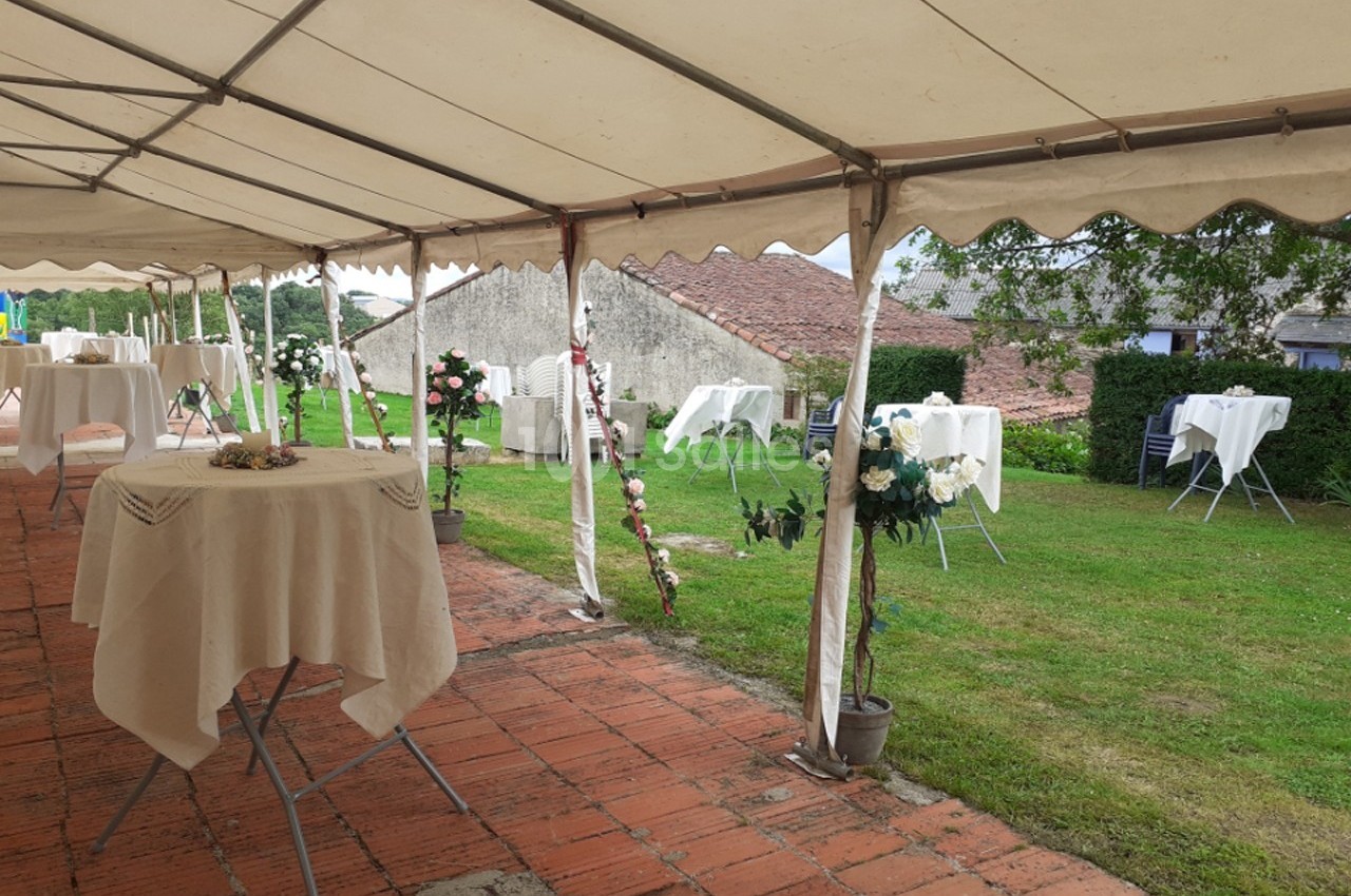 Tente blanche avec tables dressées sur une terrasse en briques, donnant sur un jardin verdoyant.