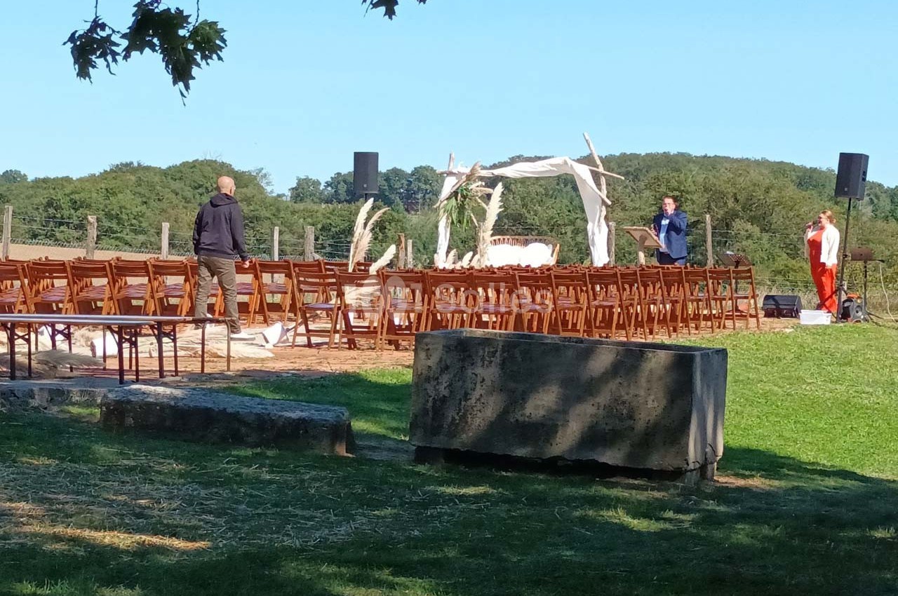 Chaises alignées en extérieur devant une arche décorée, préparatifs en cours pour un événement en plein air.