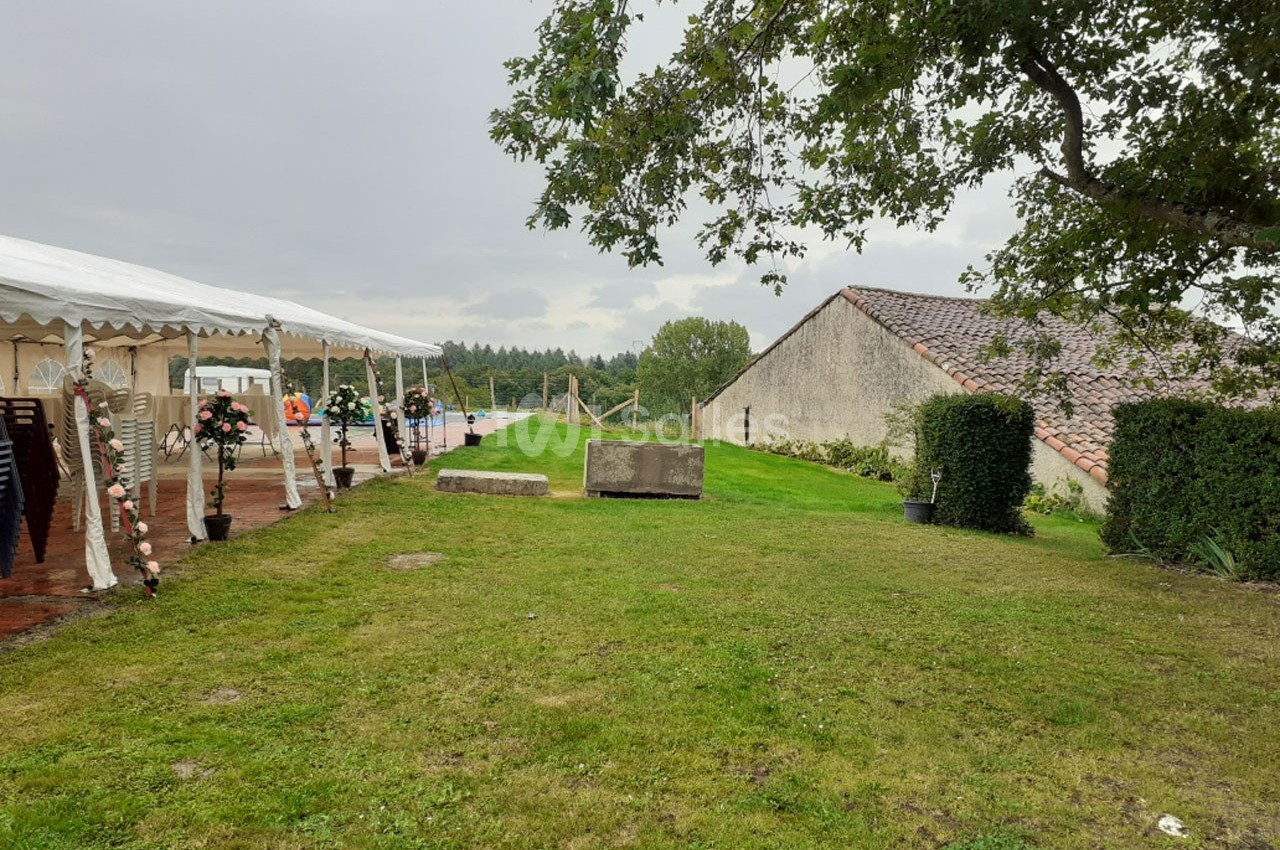 Pelouse avec une tente blanche aménagée pour un événement, entourée de bâtiments en pierre et d'arbres.