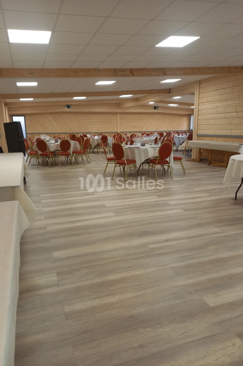 Salle de réception avec tables rondes dressées et chaises rouges, éclairée par un plafond à dalles blanches.