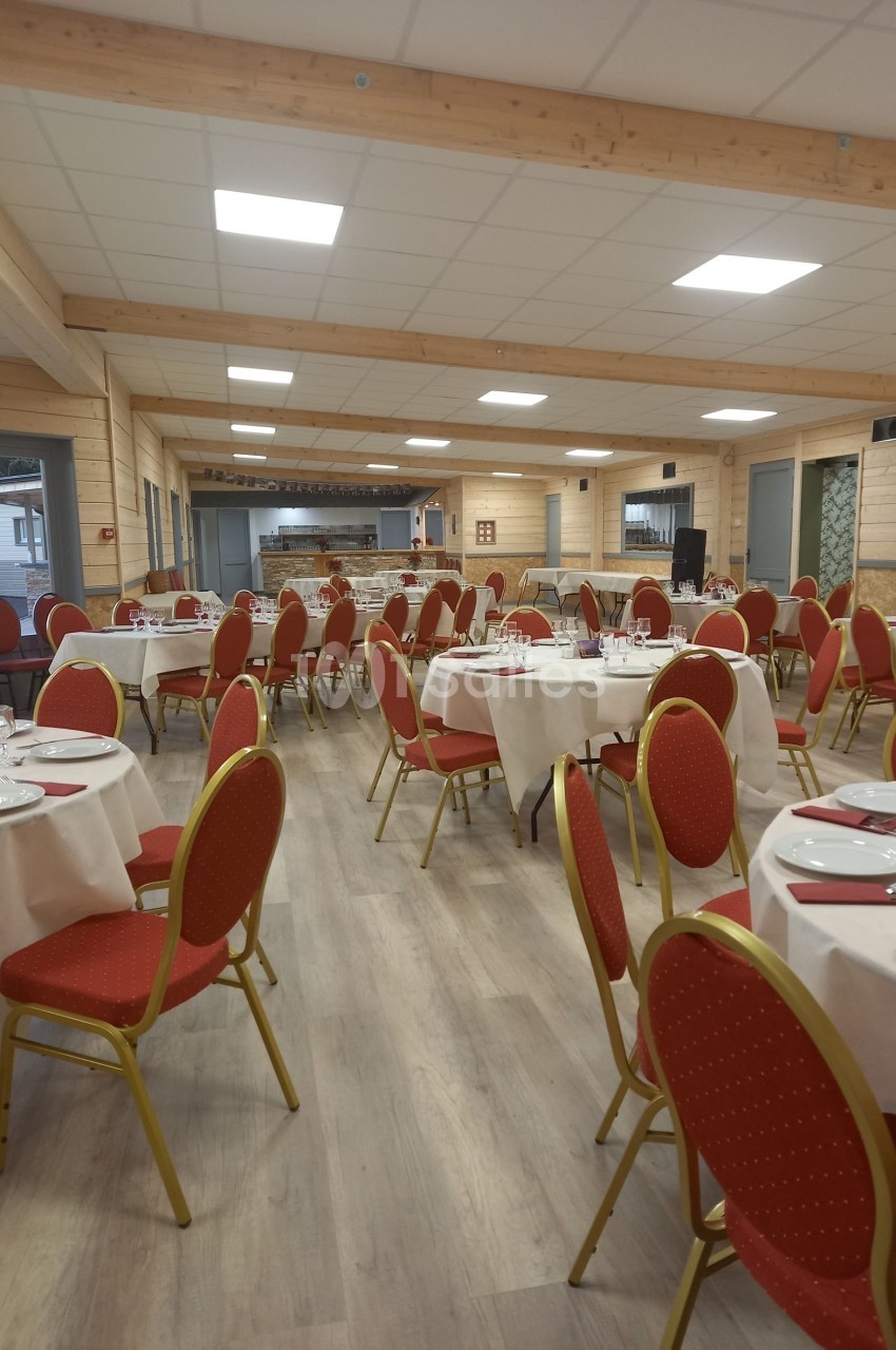 Salle de réception lumineuse avec tables rondes dressées, chaises rouges et décor en bois clair.