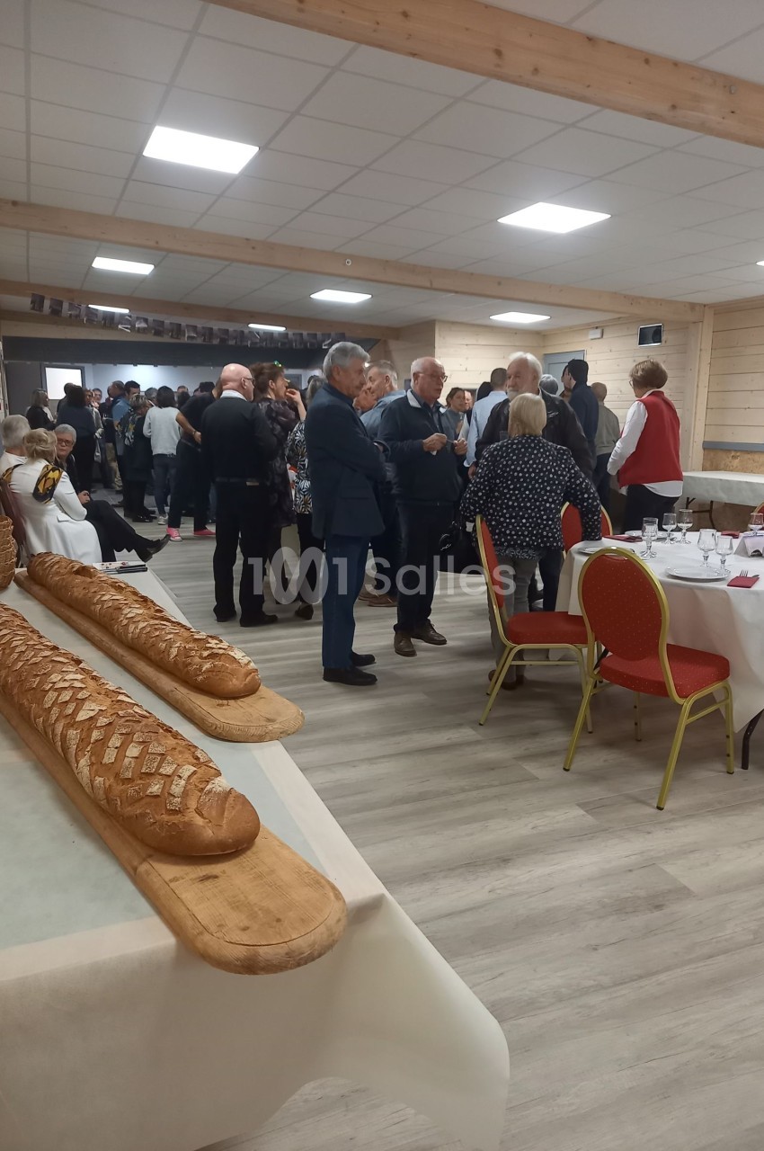 Des convives discutent dans une salle de réception avec des tables dressées et des pains disposés sur une planche au premier…