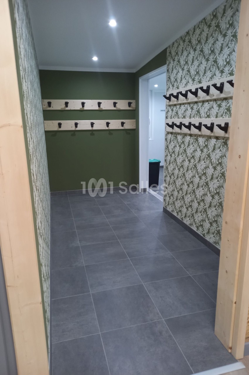 Vestiaire avec murs verts et à motifs végétaux, rangées de patères en bois, sol en carrelage gris.