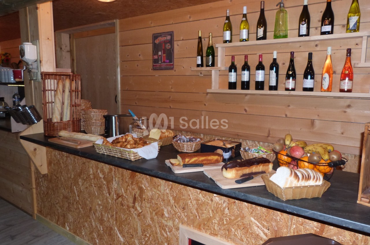 Buffet en bois avec pains, viennoiseries, fruits et bouteilles de vin alignées sur des étagères murales.