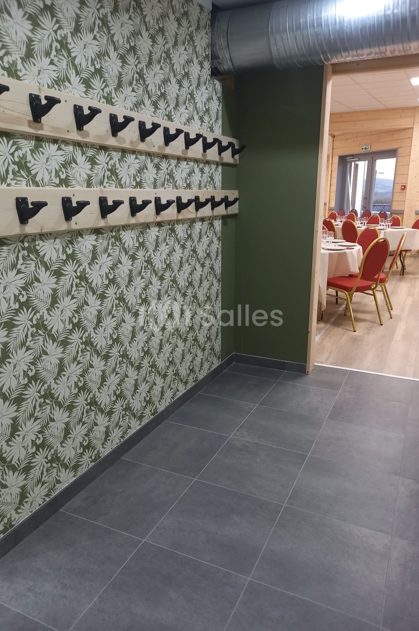 Portemanteaux muraux sur fond de papier peint végétal, avec une salle de réception visible en arrière-plan.