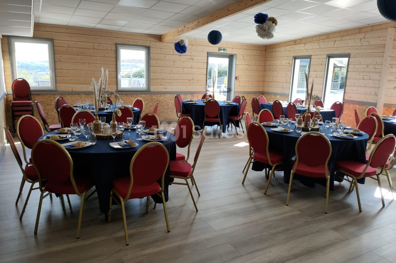 Salle décorée avec des tables rondes dressées, chaises rouges et fenêtres laissant entrer la lumière naturelle.