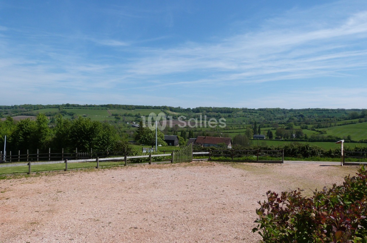 Paysage rural avec collines verdoyantes, quelques maisons dispersées et un ciel bleu parsemé de nuages légers.