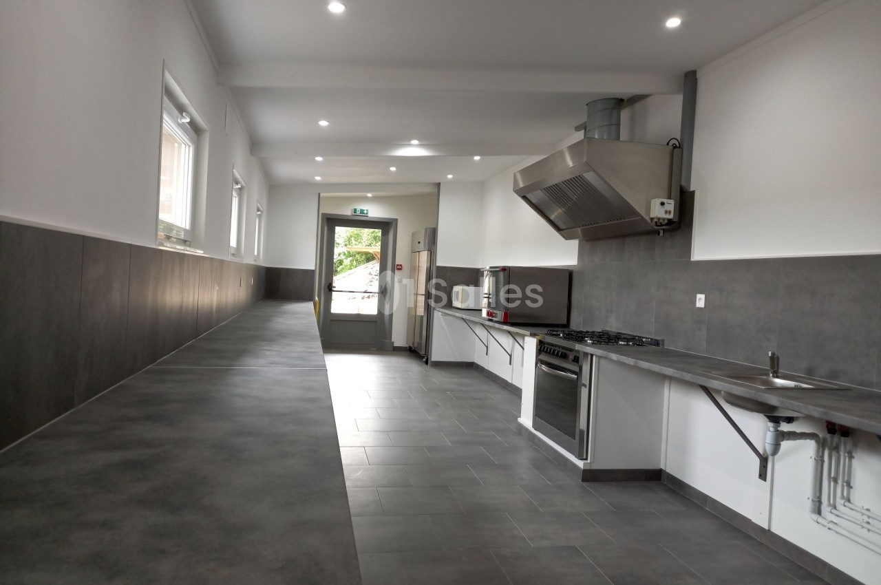Cuisine professionnelle moderne avec plan de travail long, équipements en inox et éclairage encastré.