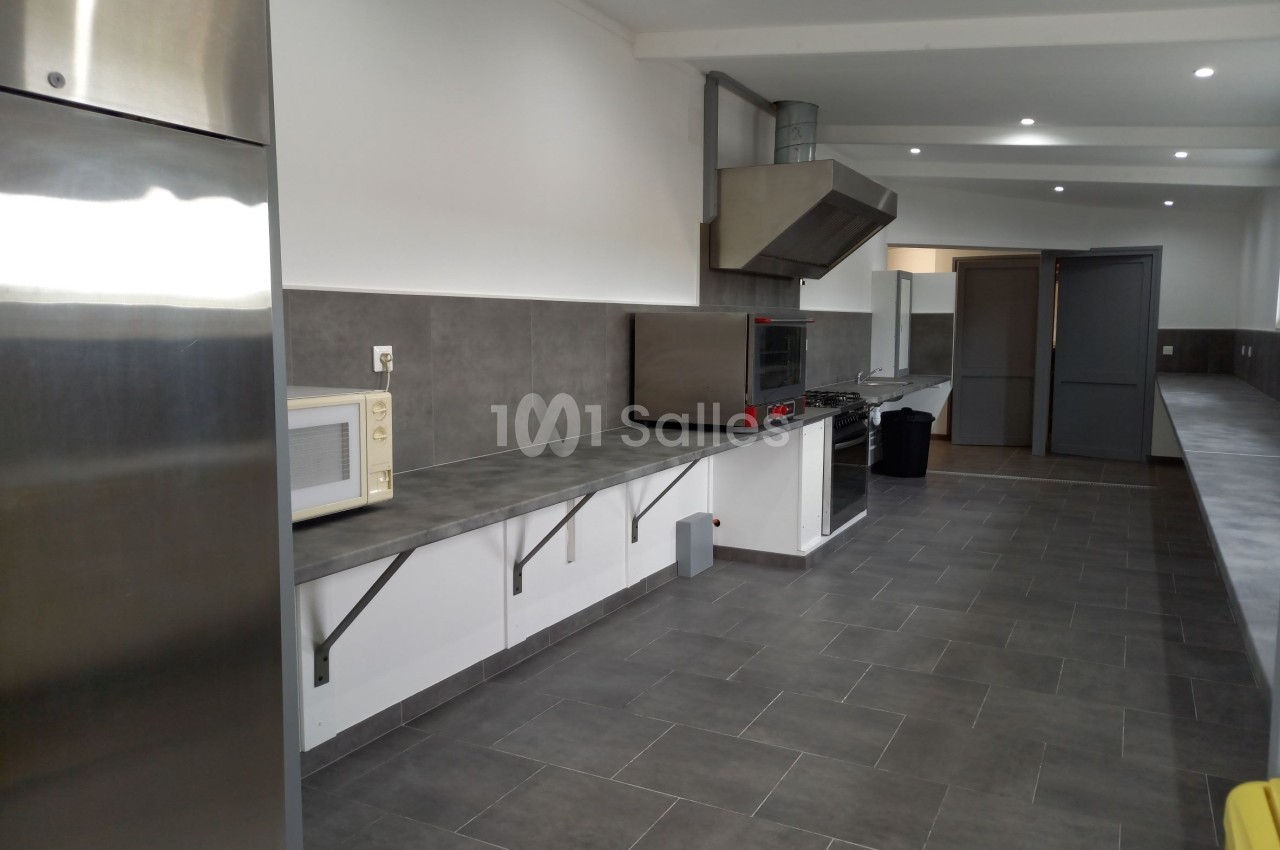 Cuisine professionnelle moderne avec plan de travail en inox, micro-ondes, four et hotte, sol en carrelage gris.