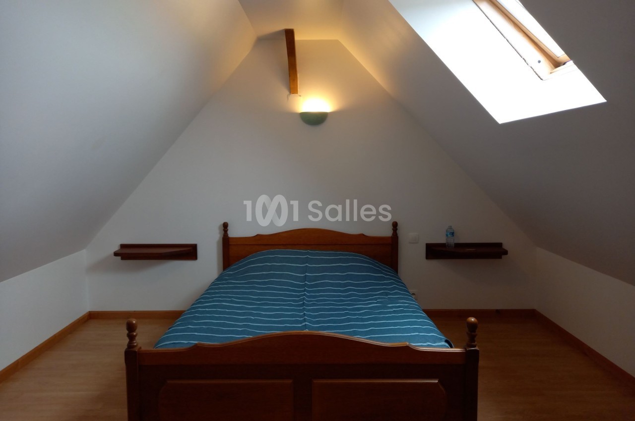 Lit en bois avec une couverture bleue dans une chambre mansardée éclairée par une fenêtre de toit.