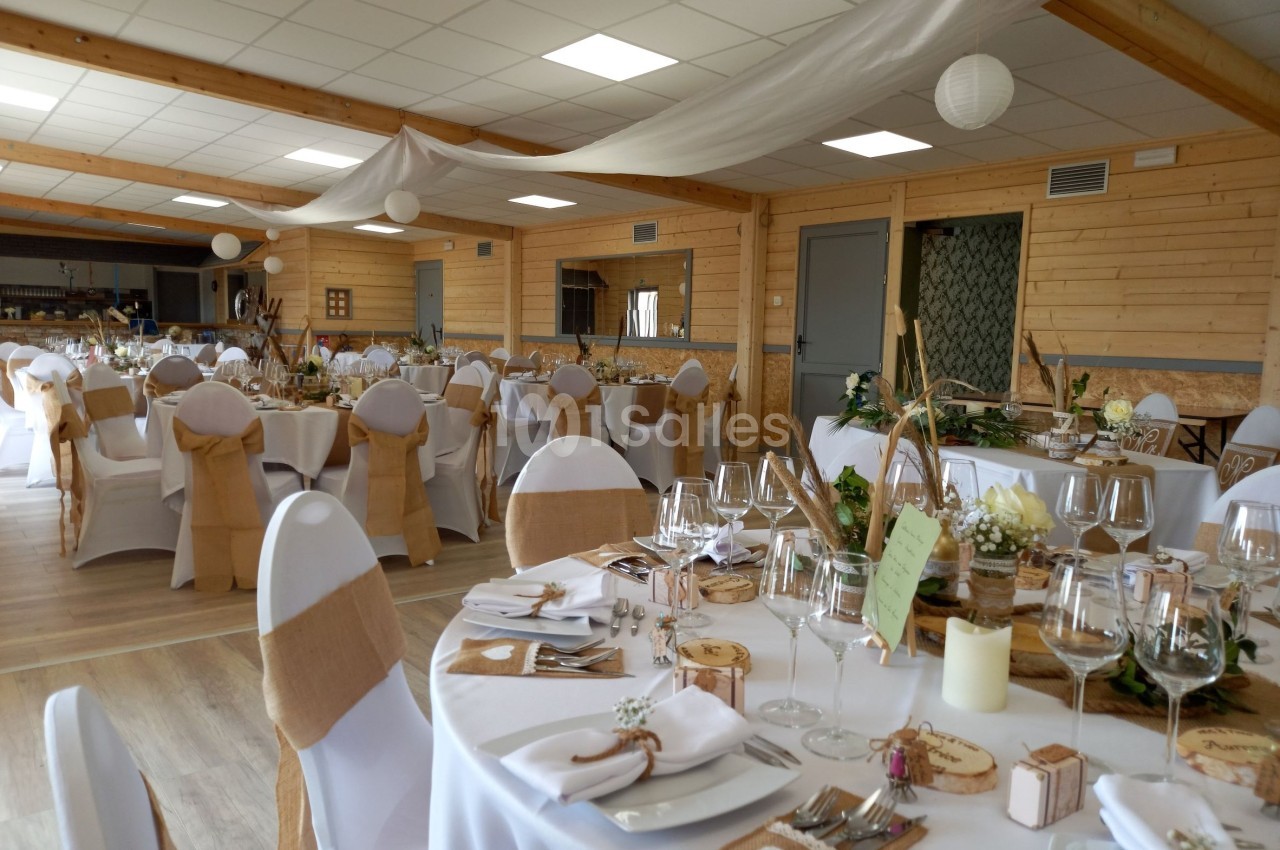 Salle de réception décorée avec des tables dressées, nappes blanches, chaises ornées de nœuds en toile de jute.