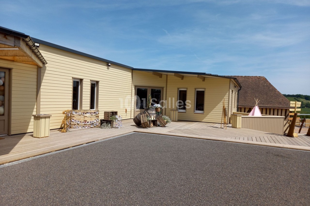 Bâtiment en bois clair avec terrasse en bois, décorations extérieures et ciel dégagé en arrière-plan.