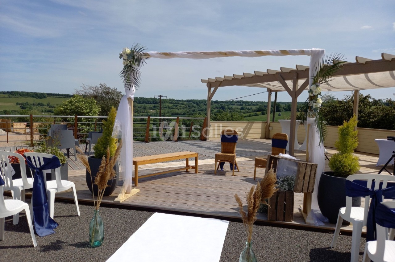 Arche décorée pour une cérémonie en plein air sur une terrasse avec vue sur la campagne environnante.