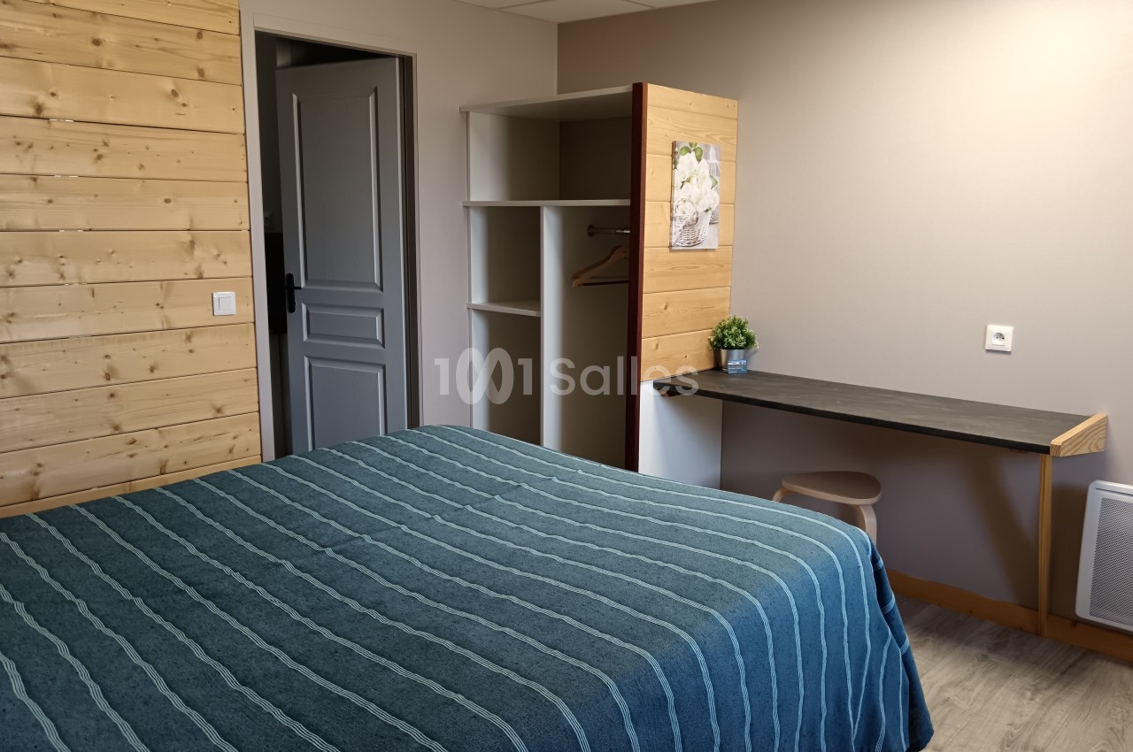 Chambre avec lit double, bureau, étagères ouvertes et mur en bois clair, dans un décor sobre et lumineux.