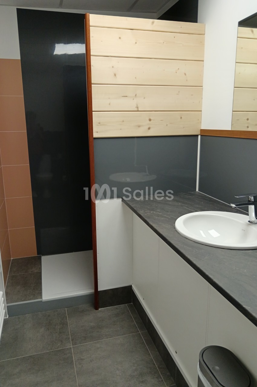 Salle de bain moderne avec lavabo, plan de travail gris, miroir, douche à paroi en bois et carrelage contrasté.