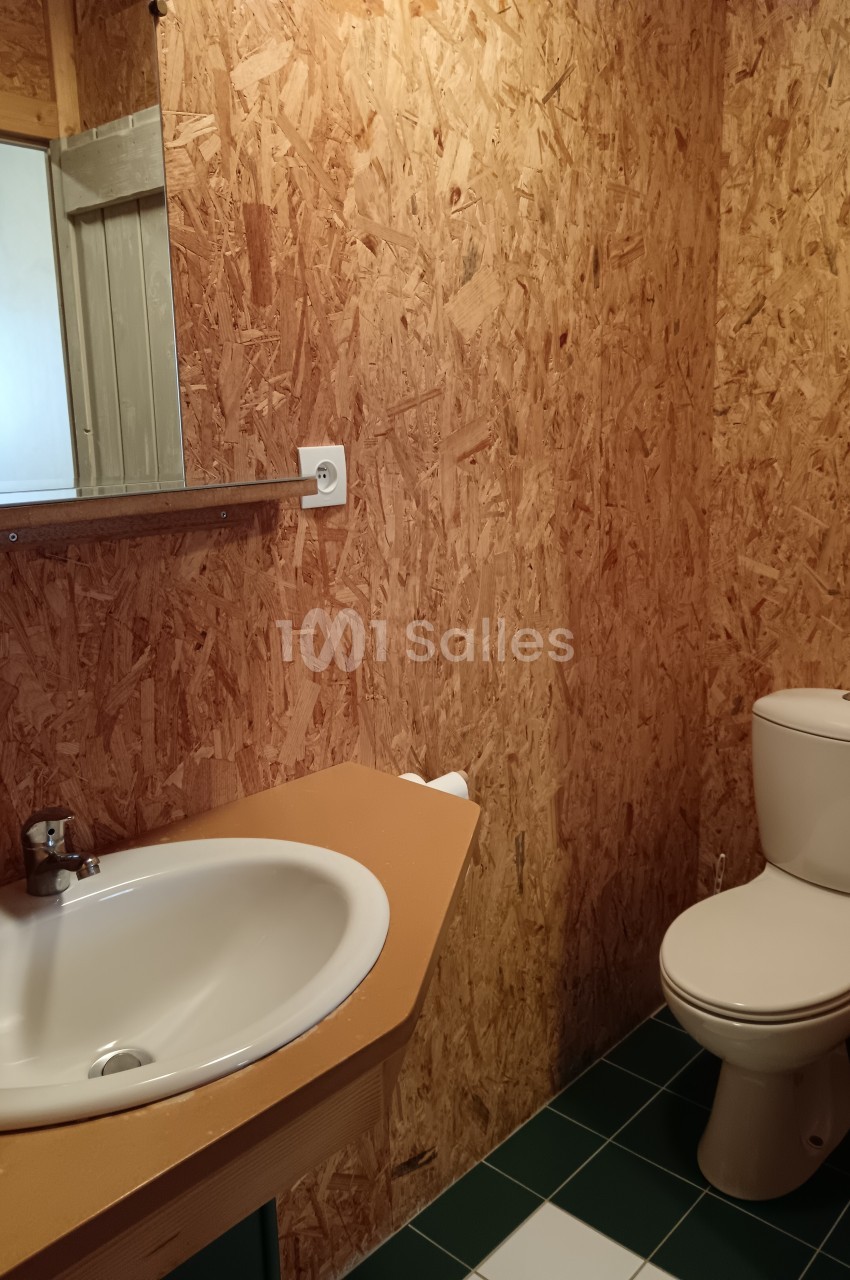 Salle de bain avec murs en panneaux OSB, lavabo avec miroir, toilettes et sol en carrelage vert.