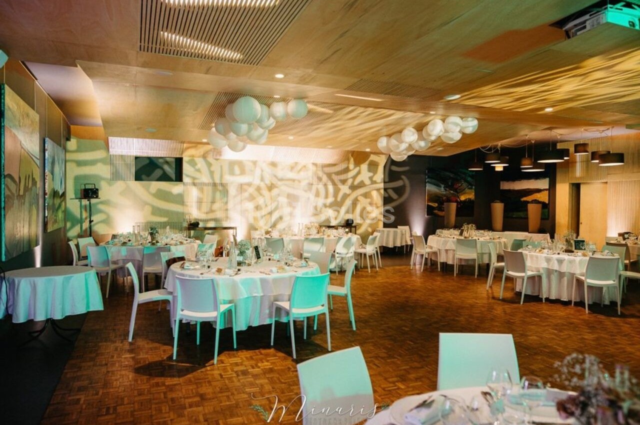 Salle de réception décorée avec des tables rondes dressées, éclairage tamisé et motifs lumineux projetés au mur.