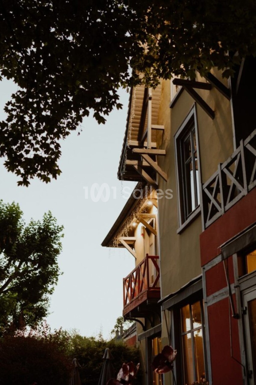 Façade d'une maison colorée avec balcons en bois, entourée de végétation sous un ciel clair en soirée.