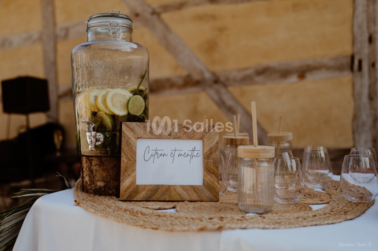 Distributeur de boisson citron et menthe avec verres en verre et pailles en bois sur une table décorée.