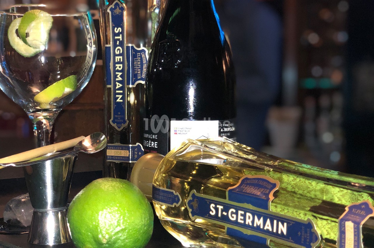 Verres, bouteille de liqueur St-Germain, lime et ustensiles de bar disposés sur un comptoir.