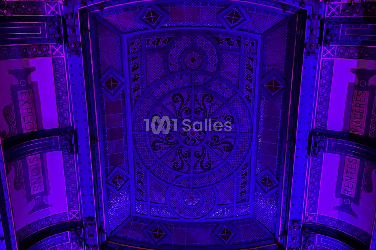 Plafond décoratif en métal orné de motifs géométriques et illuminé par une lumière violette.