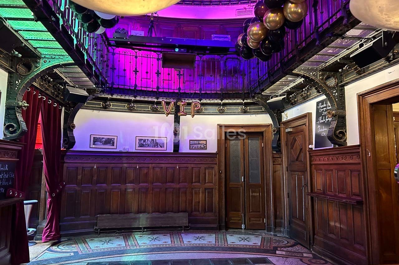 Salle décorée avec des ballons noirs et dorés, éclairage coloré, boiseries et balcon métallique en hauteur.