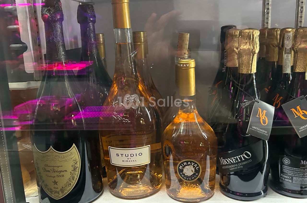 Bouteilles de vin et de champagne variées disposées sur une étagère réfrigérée.